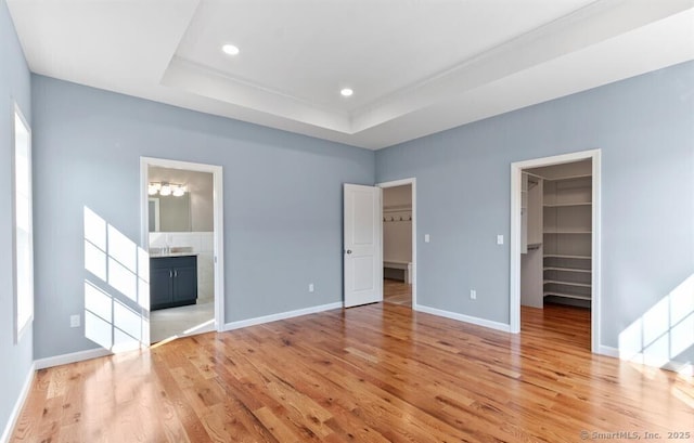 unfurnished bedroom featuring baseboards, recessed lighting, a spacious closet, a raised ceiling, and light wood-type flooring