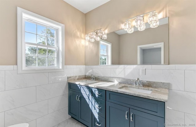 full bath with tile walls, double vanity, and a sink