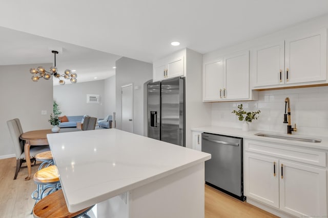 kitchen with a sink, stainless steel appliances, light wood-style floors, white cabinets, and decorative backsplash