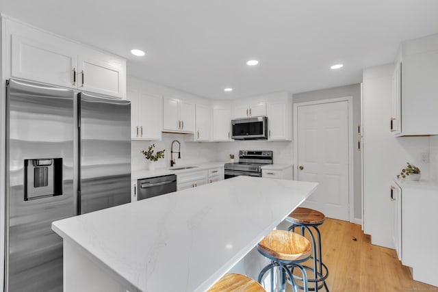 kitchen with a breakfast bar area, light wood-type flooring, white cabinets, stainless steel appliances, and a sink