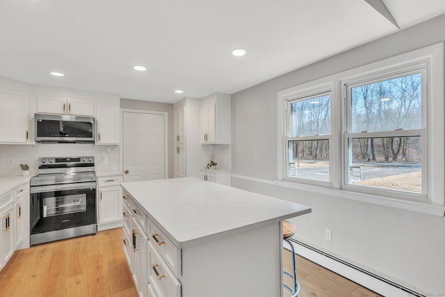 kitchen featuring light wood-type flooring, baseboard heating, appliances with stainless steel finishes, and white cabinets