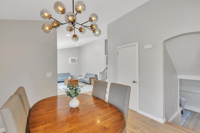 dining area featuring a wall unit AC, baseboards, lofted ceiling, stairs, and light wood-style floors