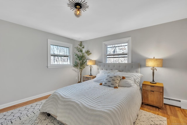 bedroom with multiple windows, wood finished floors, baseboards, and baseboard heating