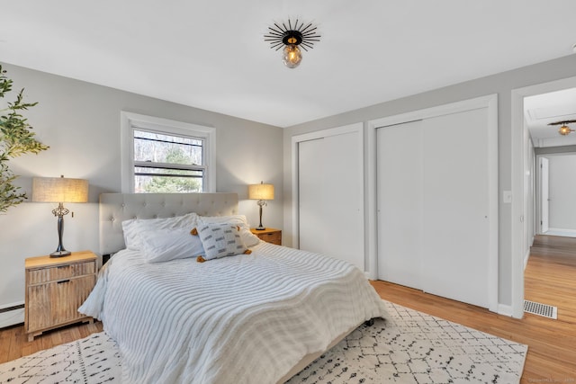 bedroom with visible vents, multiple closets, wood finished floors, and a baseboard heating unit