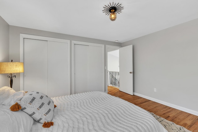 bedroom featuring baseboards, two closets, and wood finished floors