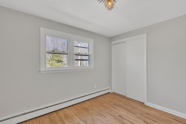 unfurnished bedroom with light wood-style flooring, a closet, and a baseboard radiator