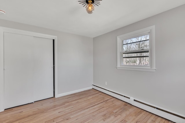 spare room with a baseboard heating unit, baseboards, and light wood-style floors