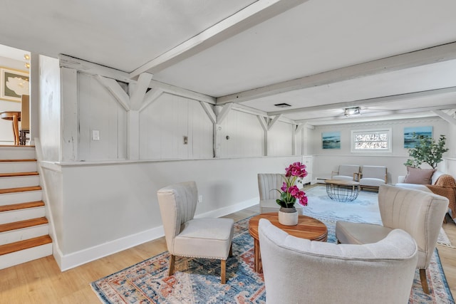 living area with visible vents, light wood-type flooring, beam ceiling, stairway, and baseboards