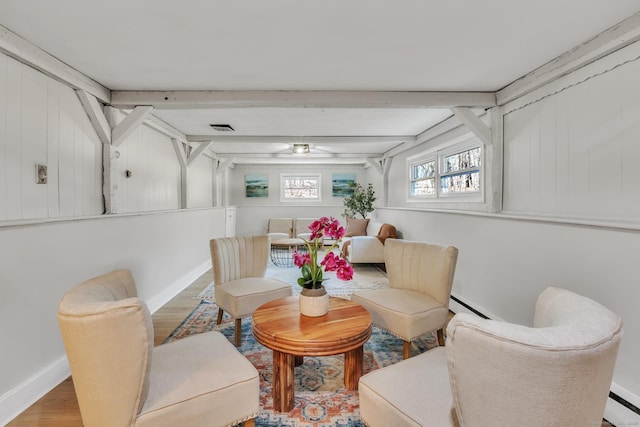 living area featuring visible vents, baseboards, beam ceiling, and wood finished floors