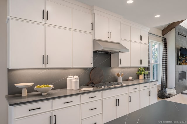 kitchen featuring under cabinet range hood, tasteful backsplash, dark countertops, white cabinetry, and stainless steel gas stovetop