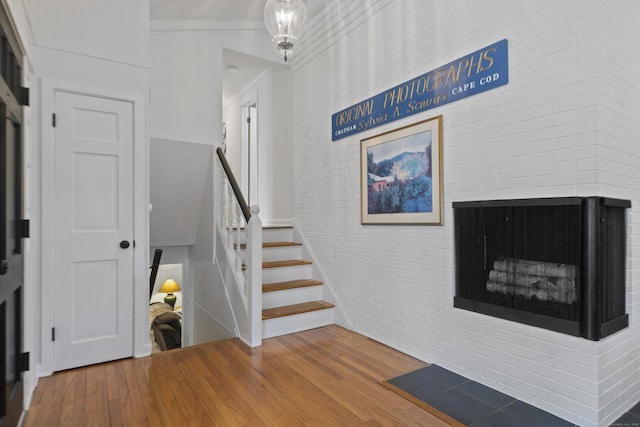 staircase featuring a brick fireplace, wood finished floors, and brick wall