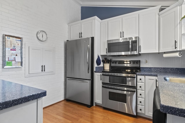 kitchen with stainless steel appliances, dark countertops, white cabinets, and light wood finished floors