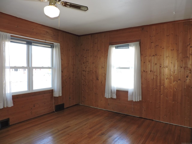 empty room featuring wooden walls, visible vents, wood-type flooring, and ceiling fan