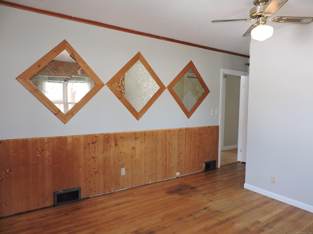 empty room with visible vents, wood finished floors, ceiling fan, and ornamental molding