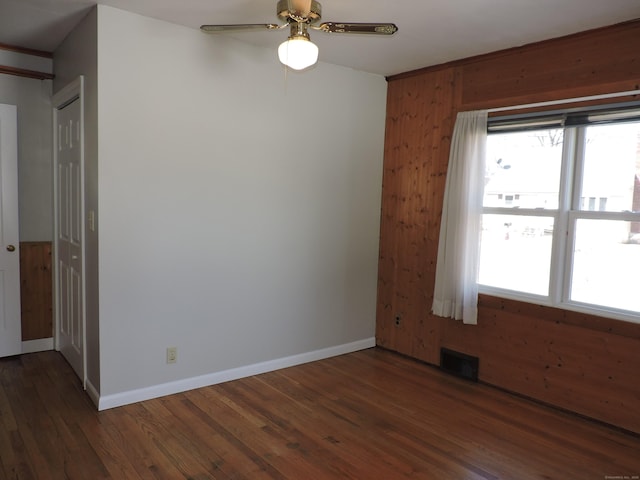 empty room featuring ceiling fan, visible vents, baseboards, and wood finished floors