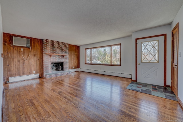 unfurnished living room with a wall unit AC, wood finished floors, and baseboard heating