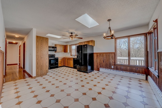 kitchen featuring a wainscoted wall, black appliances, a baseboard heating unit, wooden walls, and a skylight