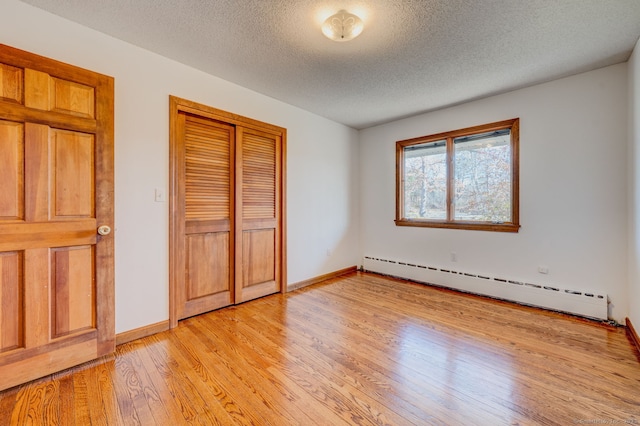 unfurnished bedroom featuring light wood-style flooring, baseboards, a closet, and a baseboard radiator