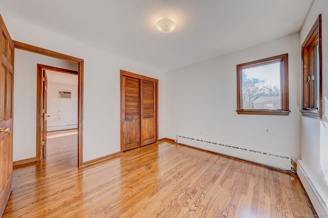 unfurnished bedroom with light wood-type flooring, a baseboard heating unit, and a closet