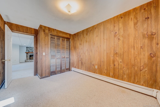 unfurnished bedroom featuring a closet, wooden walls, a fireplace, carpet flooring, and a baseboard radiator