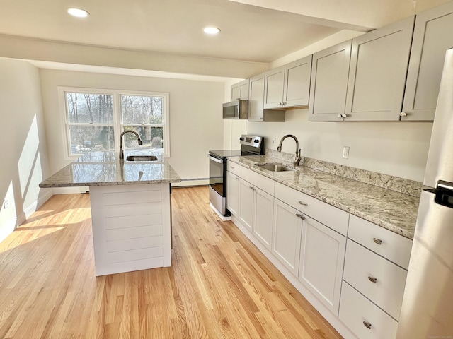 kitchen featuring light stone counters, light wood-type flooring, appliances with stainless steel finishes, and a sink