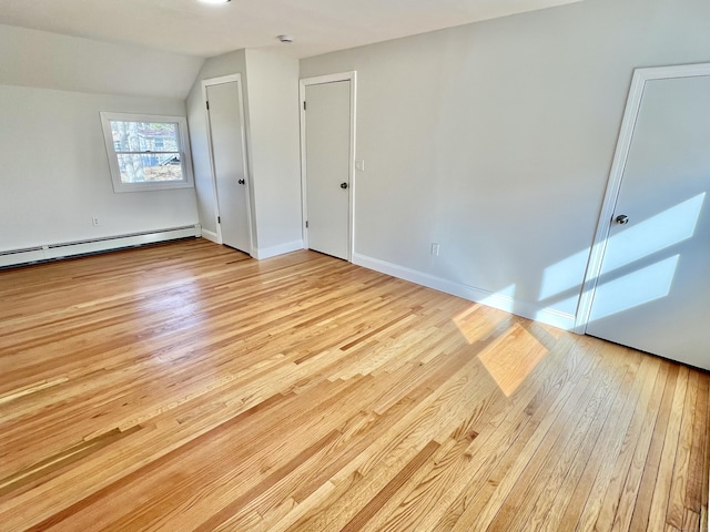 interior space featuring baseboard heating, baseboards, lofted ceiling, and light wood-style floors