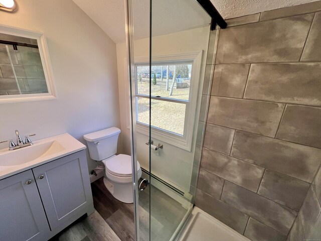 full bath with vanity, wood finished floors, tiled shower, toilet, and baseboard heating