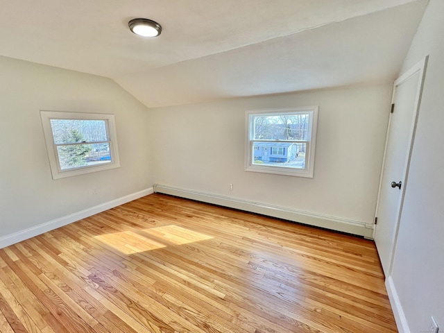 spare room featuring a wealth of natural light, light wood finished floors, baseboard heating, and vaulted ceiling