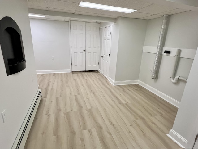 spare room featuring a paneled ceiling, baseboards, baseboard heating, and light wood finished floors