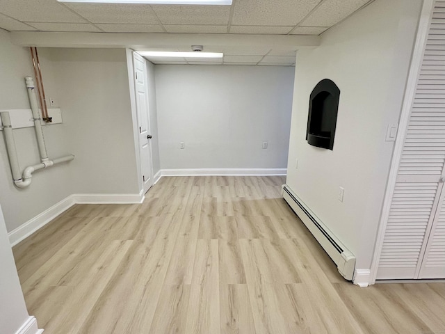 empty room with a paneled ceiling, baseboards, baseboard heating, and light wood finished floors