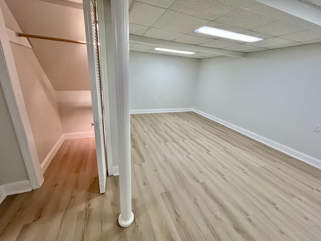 basement featuring a paneled ceiling, baseboards, and wood finished floors