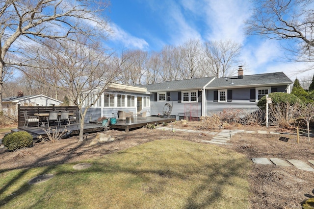 back of property with a wooden deck, roof with shingles, a lawn, a chimney, and a sunroom