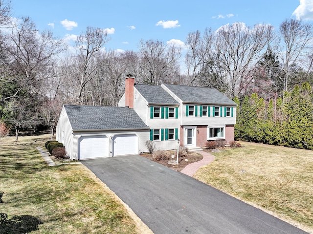 colonial house featuring a front lawn, aphalt driveway, an attached garage, brick siding, and a chimney