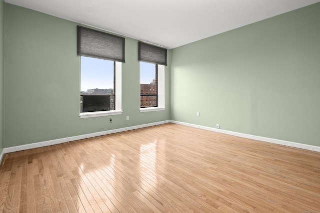 unfurnished room with a city view, light wood-style flooring, and baseboards