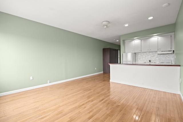 unfurnished living room featuring recessed lighting, light wood-style flooring, baseboards, and a sink