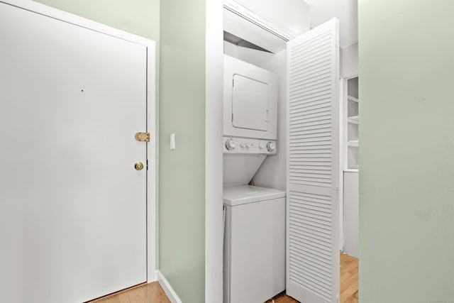 washroom featuring laundry area, stacked washer / dryer, baseboards, and light wood finished floors