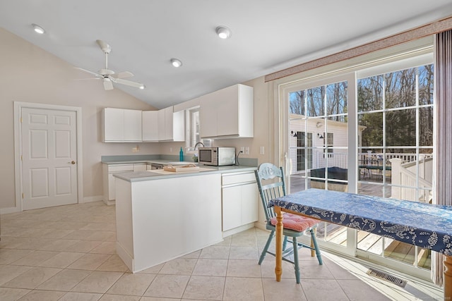 kitchen featuring white cabinets, light tile patterned flooring, light countertops, lofted ceiling, and white microwave