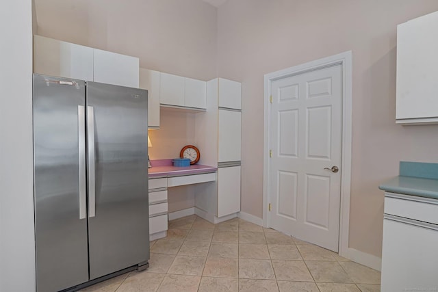 kitchen featuring light tile patterned flooring, white cabinets, freestanding refrigerator, and baseboards