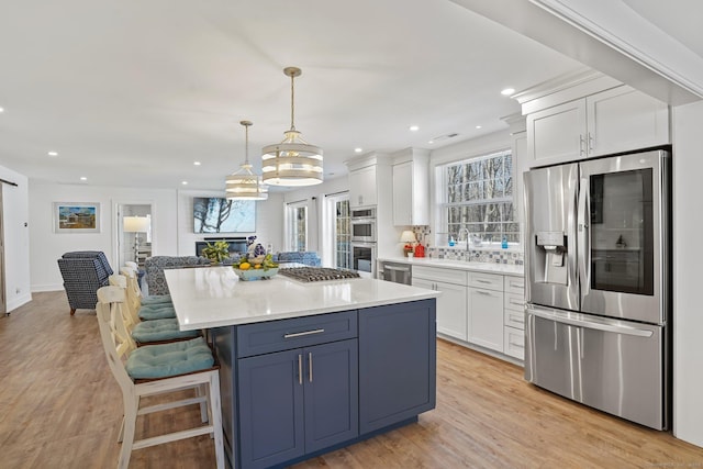 kitchen with a breakfast bar area, stainless steel appliances, white cabinets, light wood-type flooring, and a center island