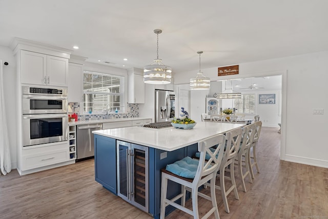 kitchen featuring beverage cooler, white cabinets, light wood-style floors, appliances with stainless steel finishes, and blue cabinets