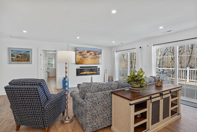 living room with a glass covered fireplace, visible vents, and wood finished floors