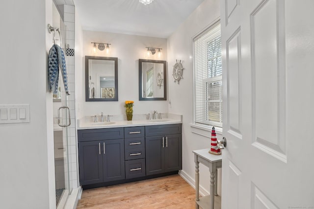 bathroom featuring a sink, wood finished floors, a stall shower, and double vanity