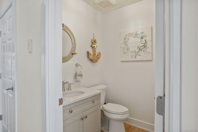 half bathroom with visible vents, baseboards, toilet, wood finished floors, and vanity