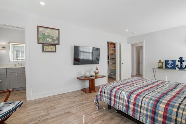 bedroom with light wood-type flooring, a walk in closet, a sink, recessed lighting, and baseboards