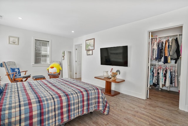 bedroom with a spacious closet, baseboards, recessed lighting, wood finished floors, and a closet