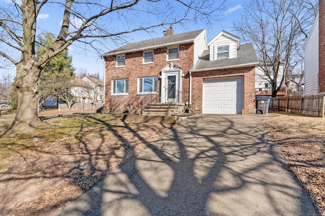 colonial home featuring brick siding, fence, aphalt driveway, a chimney, and a garage