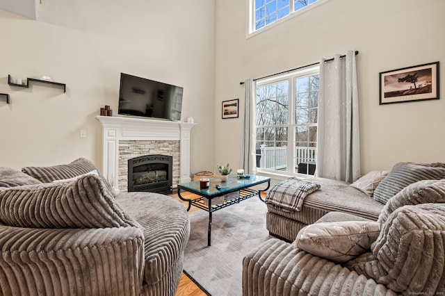 living room featuring a stone fireplace, a towering ceiling, and light wood finished floors