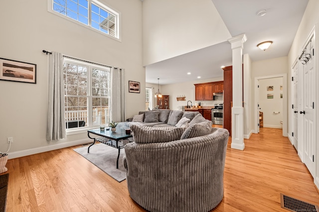 living area with visible vents, baseboards, decorative columns, light wood-style floors, and a towering ceiling