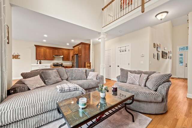 living room featuring a towering ceiling, light wood-style floors, recessed lighting, and ornate columns