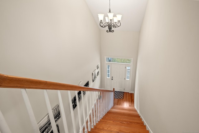 stairway featuring lofted ceiling, wood finished floors, baseboards, and a chandelier